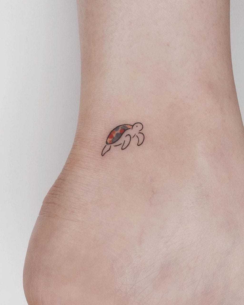 Tiny minimalist turtle tattoo with red and grey shell on the ankle