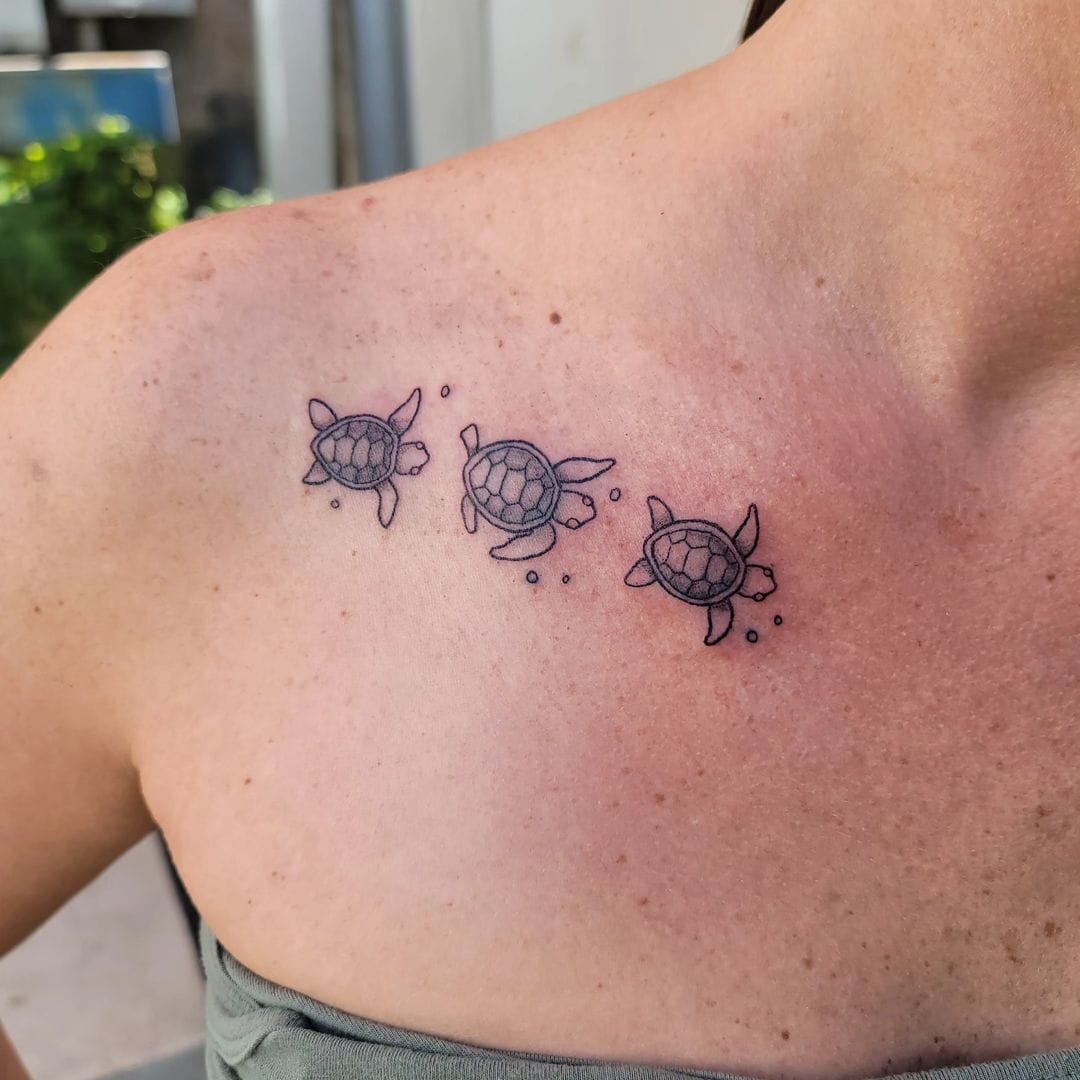 Three small fine-line turtles walking across the collarbone