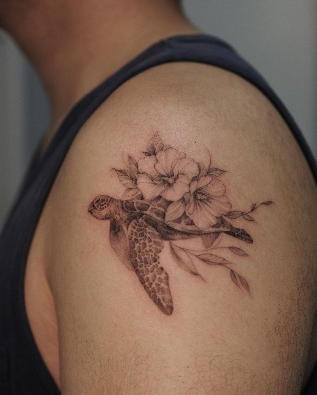 Fine-line sea turtle tattoo with hibiscus flowers on a shoulder