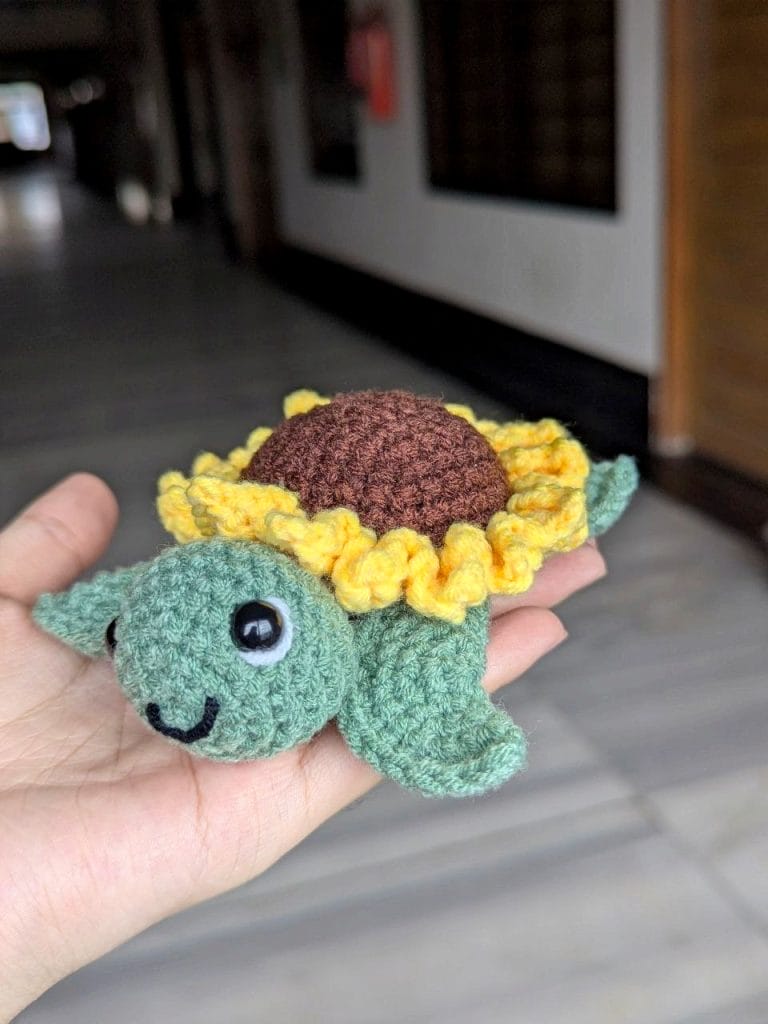 Finished sunflower turtle with bright yellow petals crowning the dark brown shell, light green head and flippers, and embroidered face