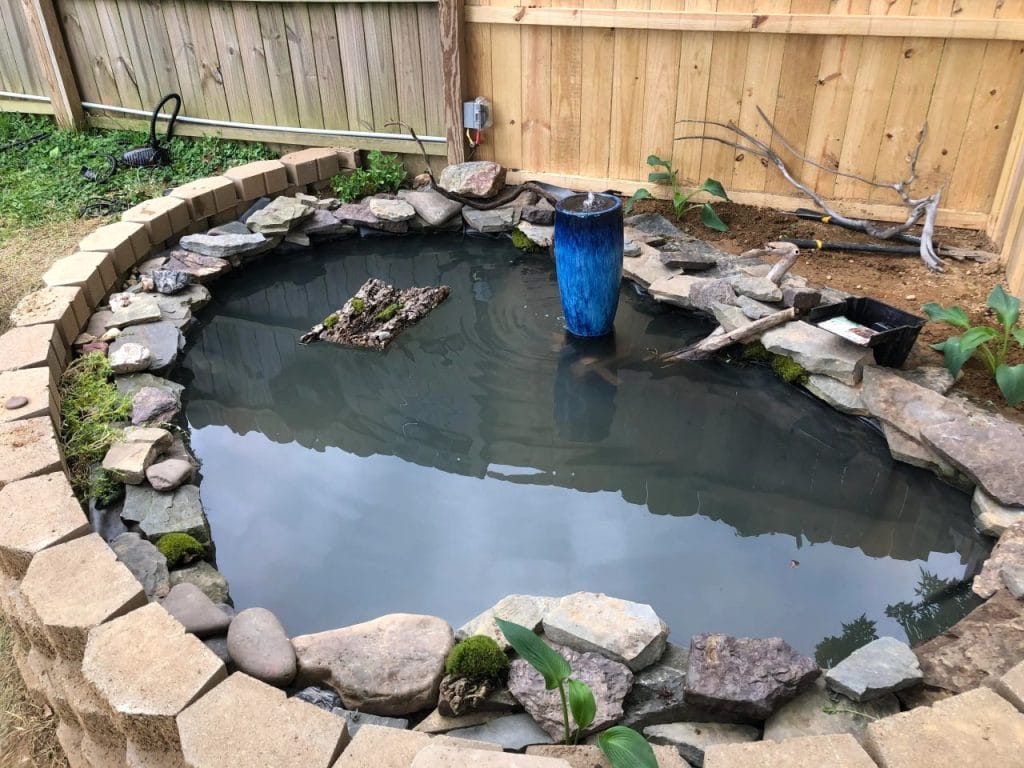 Outdoor turtle pond with stacked stone retaining wall and blue ceramic fountain vase