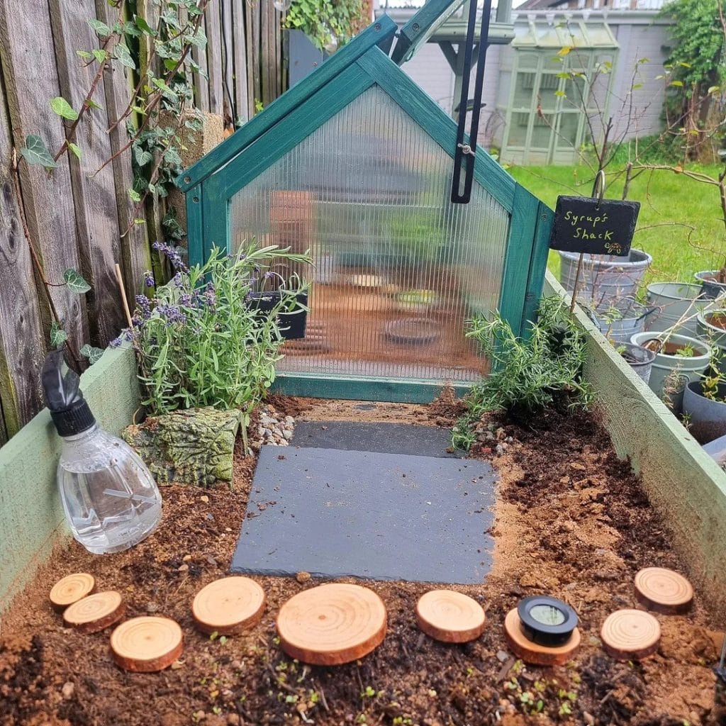 Greenhouse retreat tortoise garden with a mini greenhouse, slate basking tile, wood-slice path, and herb plantings