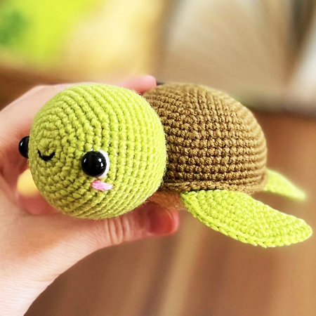 Cute green kawaii crochet sea turtle with big eyes, a sleepy wink and pink cheeks