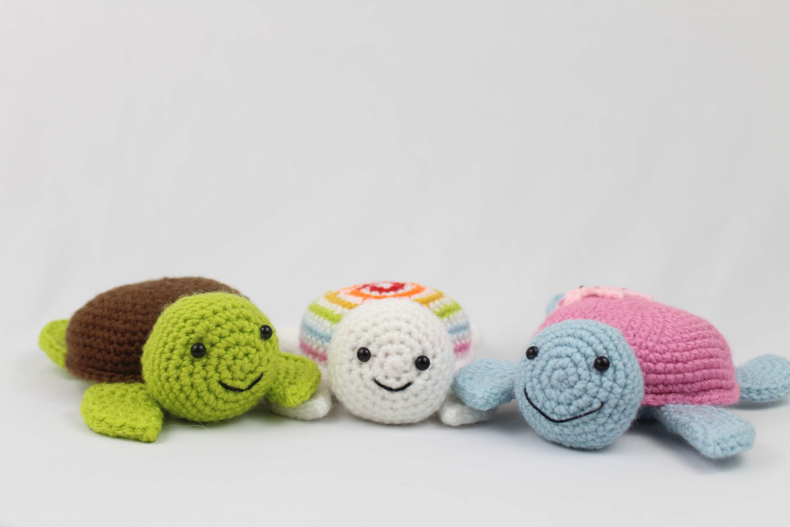 Three smiling kawaii crochet turtles including one with a rainbow striped shell