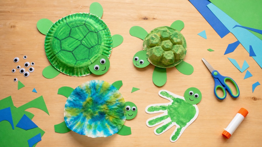 A collection of easy kid-made sea turtle crafts including a paper plate turtle, egg carton turtle, and handprint turtle arranged on a table