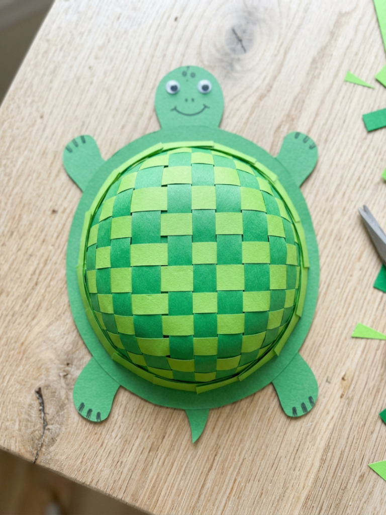 Turtle craft with a woven paper shell made from over-and-under green paper strips in a checkerboard pattern