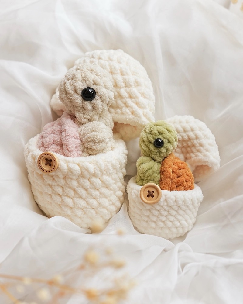 Two mini crochet baby tortoises hatching out of white crocheted egg shells
