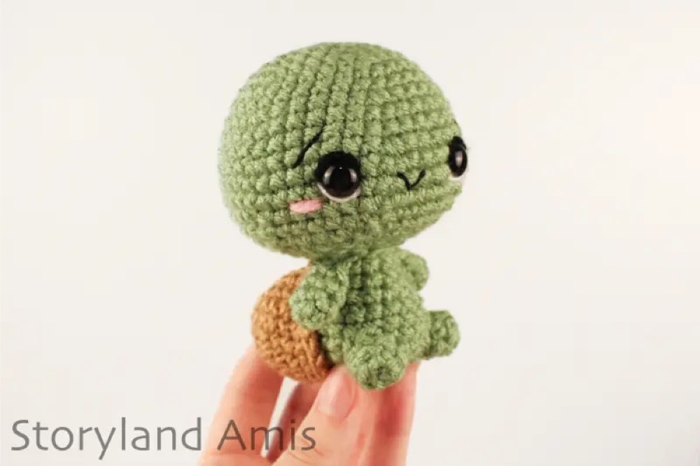 Mini green crochet tortoise with a brown shell held between two fingers