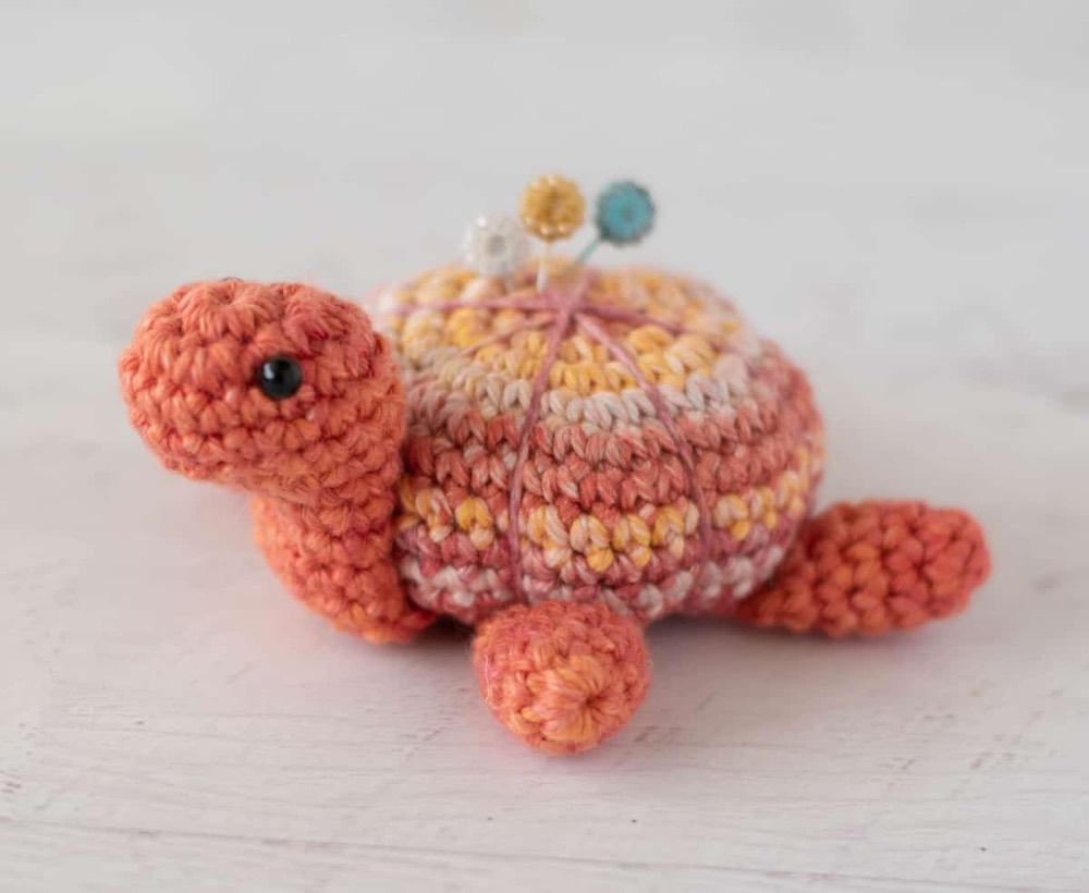 Small orange crochet turtle pincushion with sewing pins in its shell