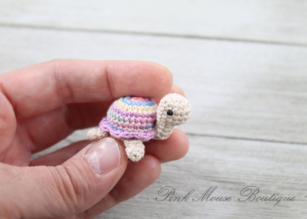 Tiny thread crochet turtle with a pastel striped shell held in a hand for scale