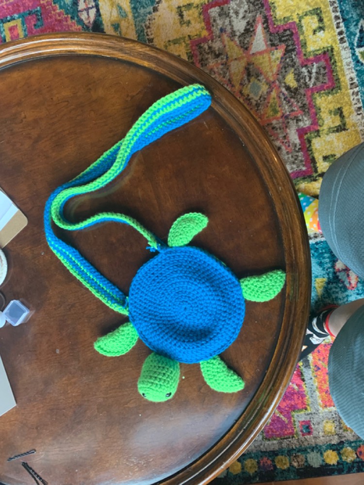 Blue and green crochet turtle shoulder bag with a long strap on a wooden table
